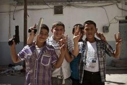 Four Syrian boys hold up toy guns and show the peace sign