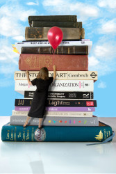 Miniature woman holding a red balloon in front of a tower of books