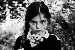 A young girl looks to camera, she is holding scissors across her plait