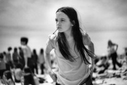 A young girl with a cigarette pulls up her jeans on the beach